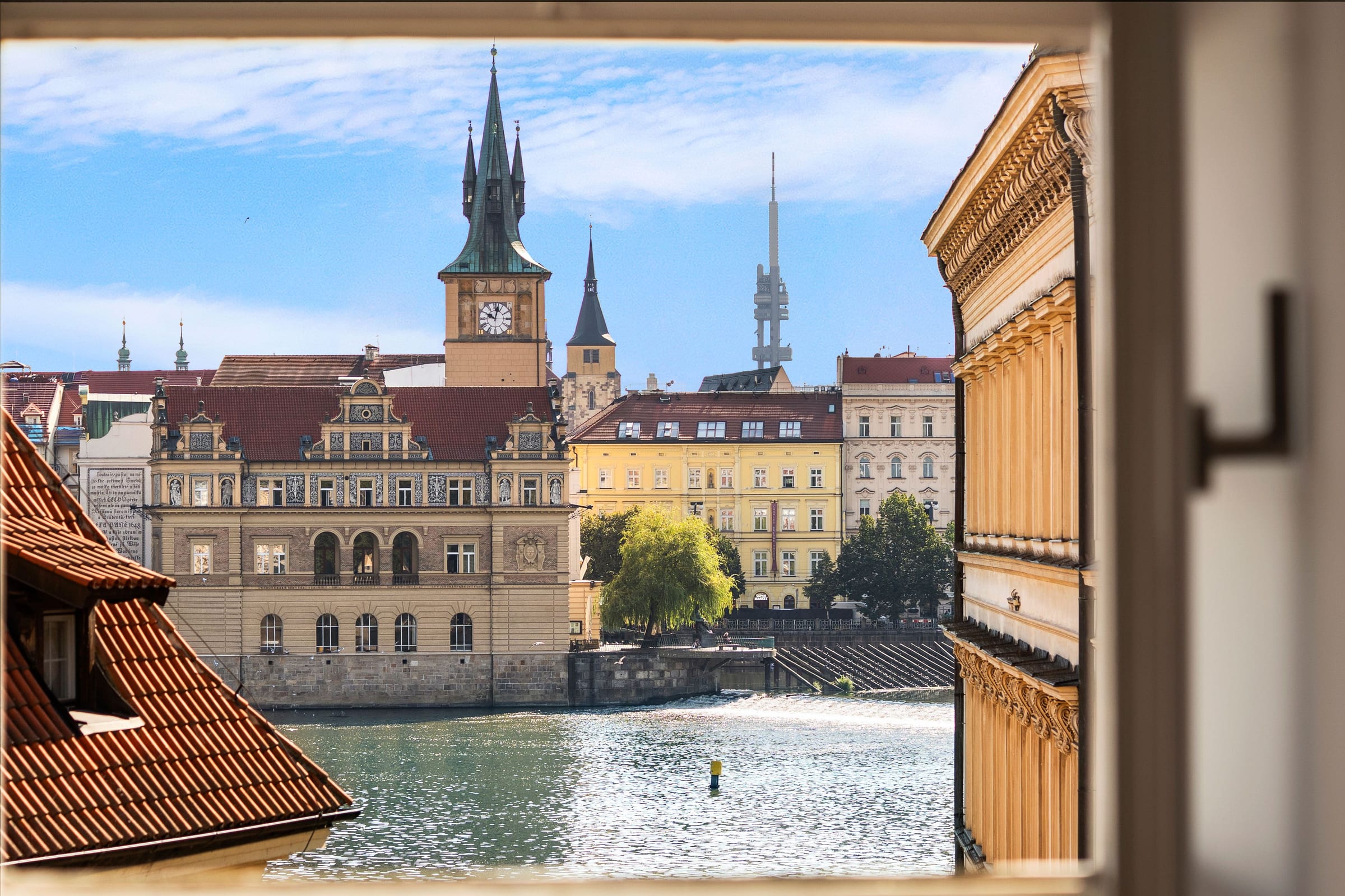 Blick aus dem offenen Fenster über die Moldau auf das Smetana-Ufer und den Altstädter Wasserturm